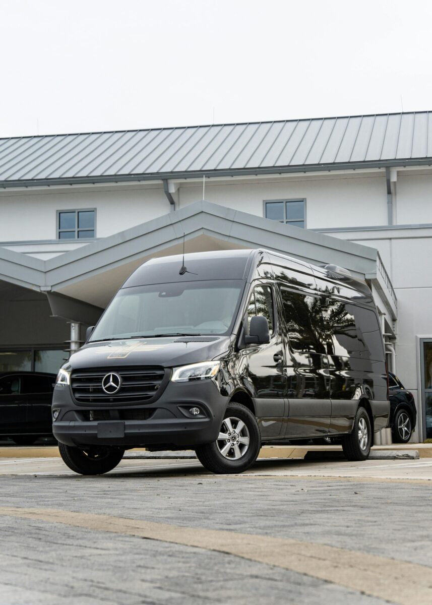 Black Mercedes-Benz Sprinter van parked in front of a modern building under a cloudy sky.